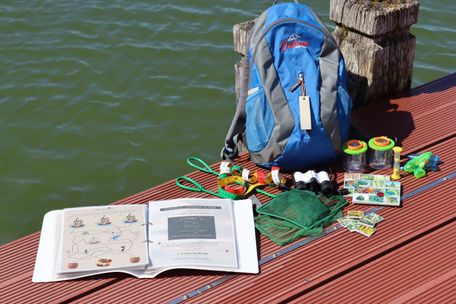 Alpseerallye Rucksack mit ausgelegtem Inhalt auf dem Erlebnissteg am Großen Alpsee.