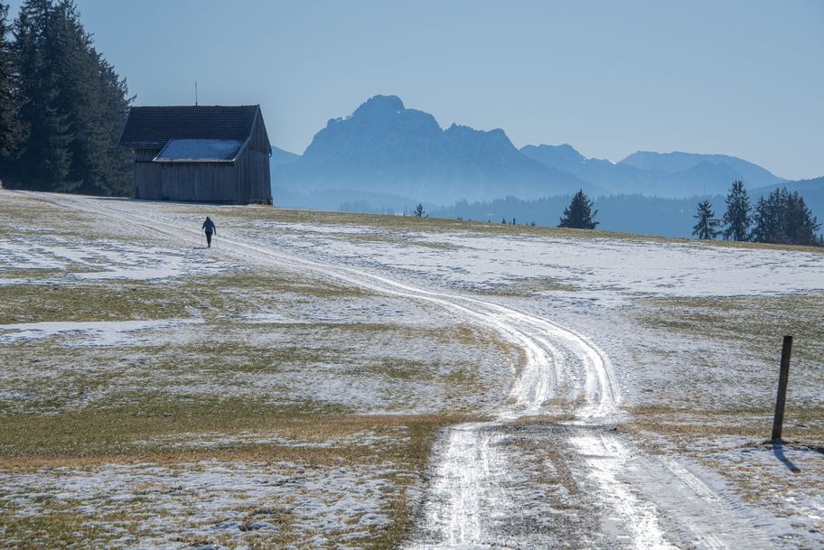 Teils vereister Forstweg über die Felder mit Bergpanorama.