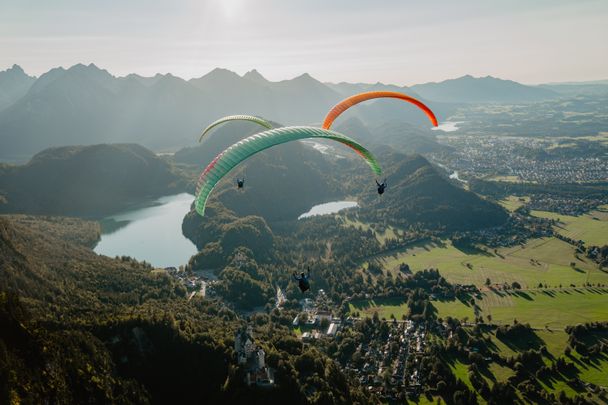 Drei Paragleiter über Schwangau mit Schloss Neuschwanstein und dem Alpsee