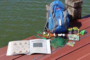 Alpseerallye Rucksack mit ausgelegtem Inhalt auf dem Erlebnissteg am Großen Alpsee.