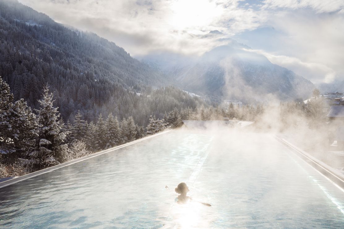 frau-im-infinity-pool-panorama-wasser-nebel-winter-berge-ifen-hotel-kleinwalsertal